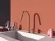 Küchenarmatur in edlem Design von Ideal Standard, mit zwei Auslässen und einem Edelstahl-Finish, montiert an einem weißen Spülbecken vor einer farbigen Wand.